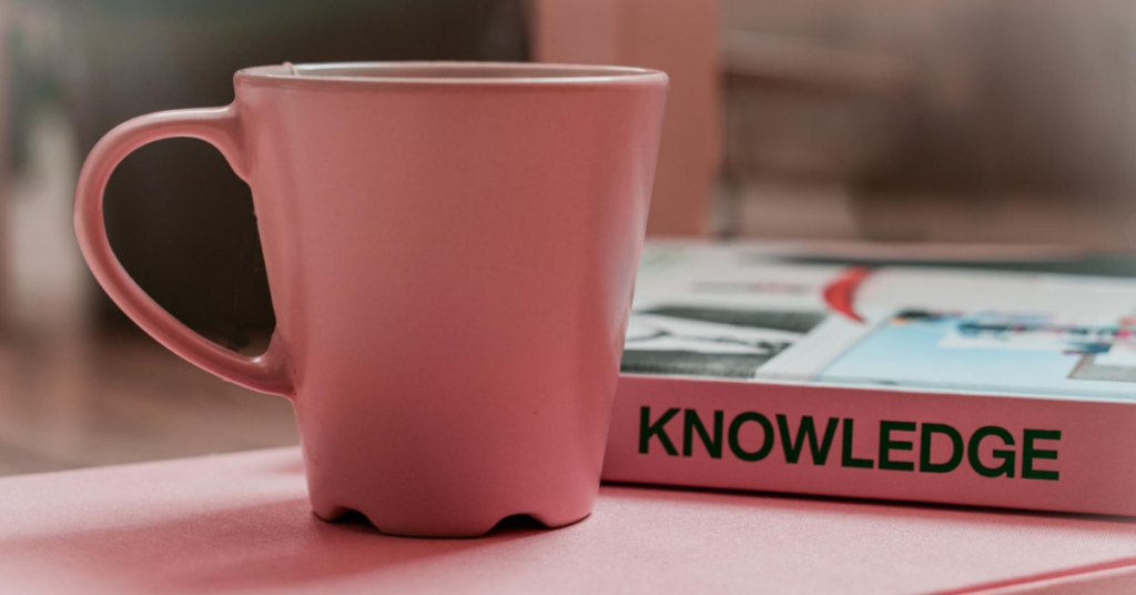 Pink mug, tab and book that says 'knowledge'.