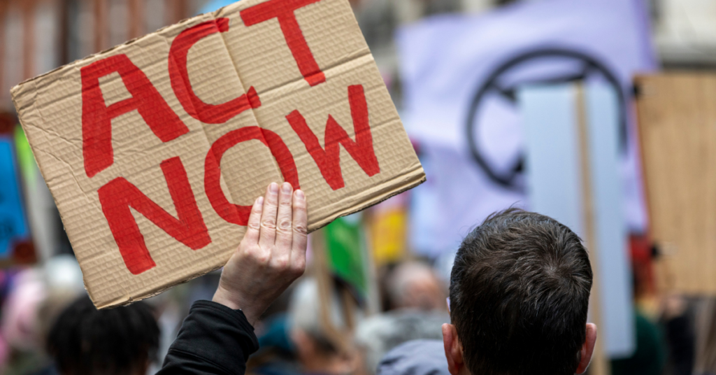 Person holding 'Act Now' protest banner