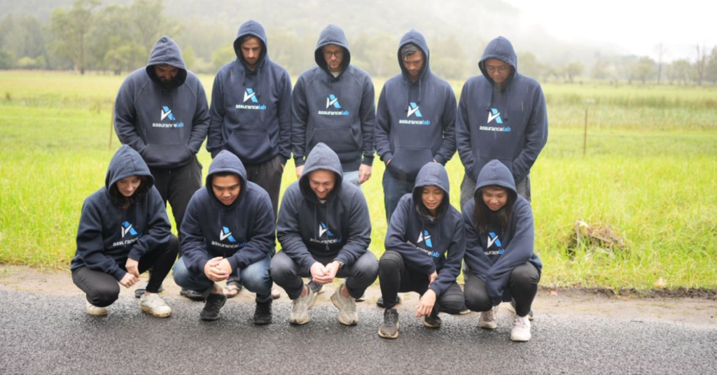 AssuranceLab team in matching hoodies looking down at the ground
