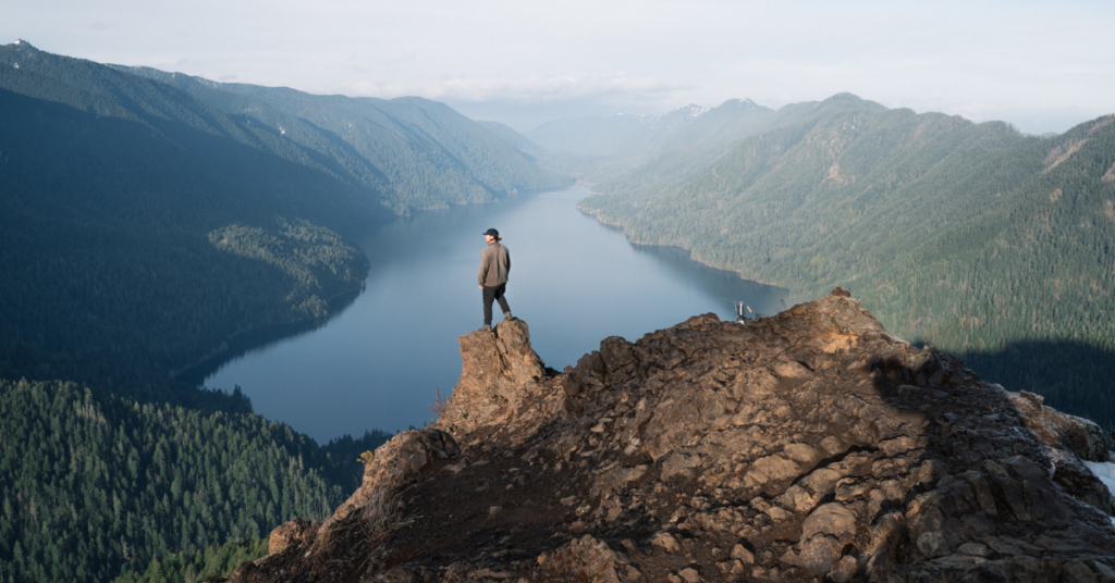 One person standing on a mountain's edge overlooking a body of water.