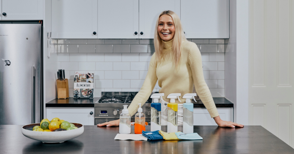 Person smiling at camera with Pleasant State cleaning products lined up on kitchen bench