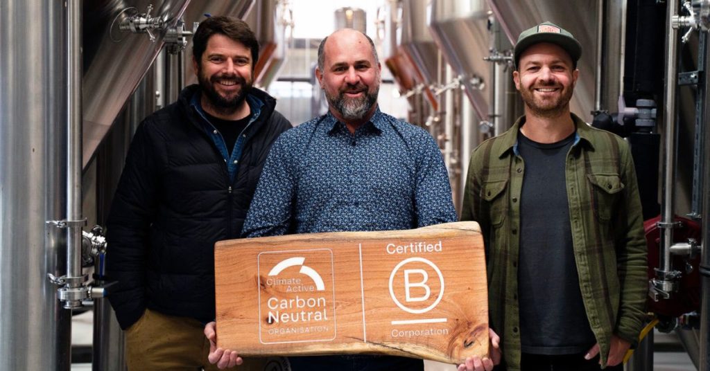 three men from capital brewing holding a large piece of wood engraved with the Climate Active Carbon Neutral Organisation and Certified B Corporation logos engraved