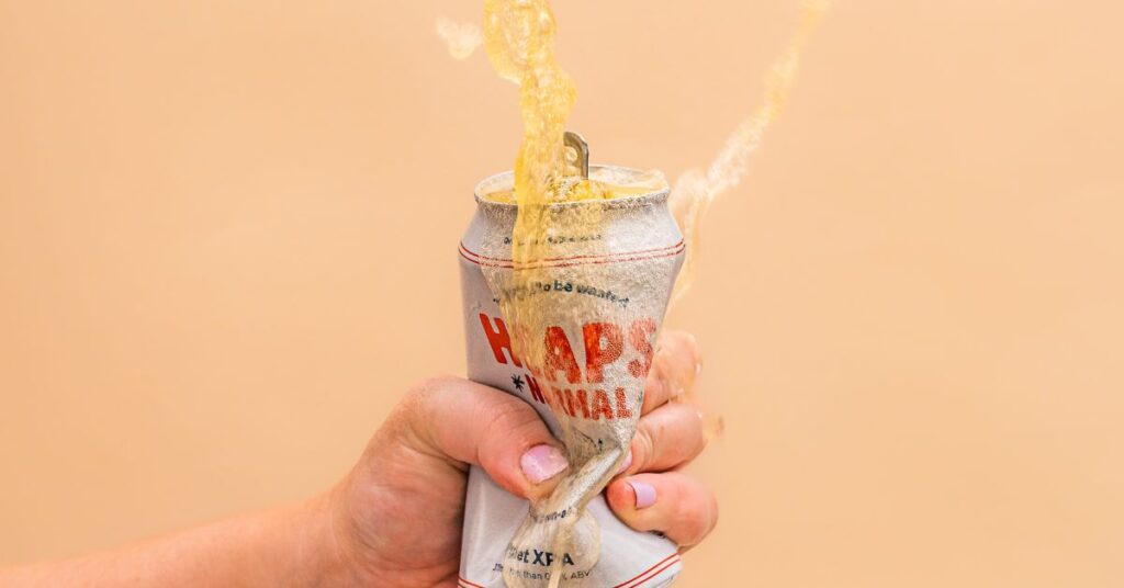 A hand squeezing a Heaps Normal can. Beer is exploding everywhere.