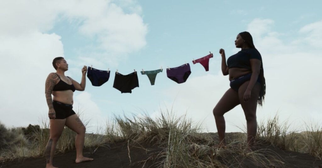 Two women holding AWWA underwear on a washing line
