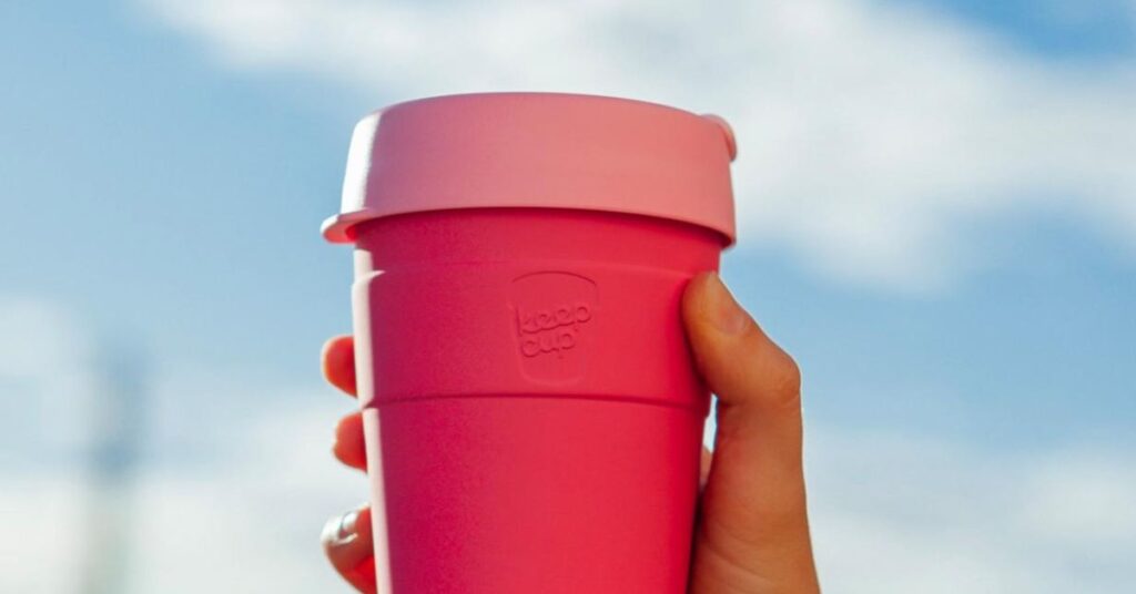 A pink KeepCup held up to the sky 
