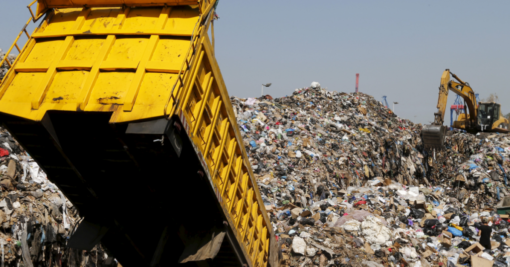 A picture of landfill with a yellow truck dumping waste