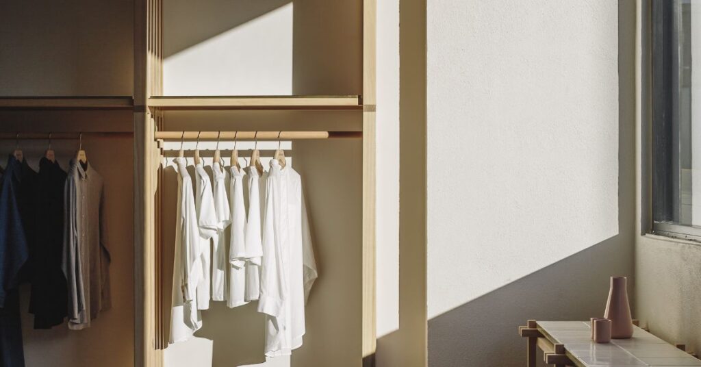 White Kowtow shirts hanging in a wooden wardrobe