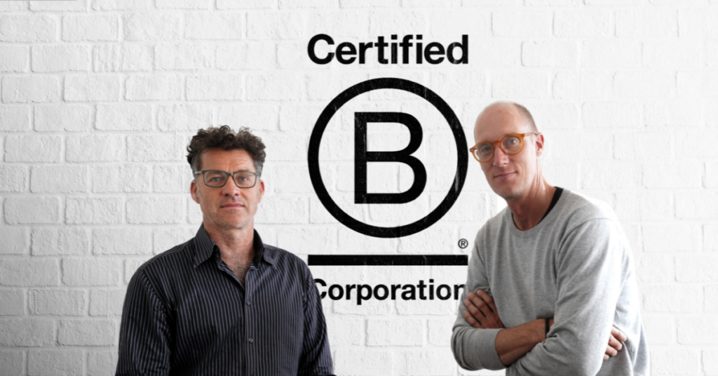 The Hallway founders sitting looking directly at camera, white brick background and Certified B Corporation logo in the background