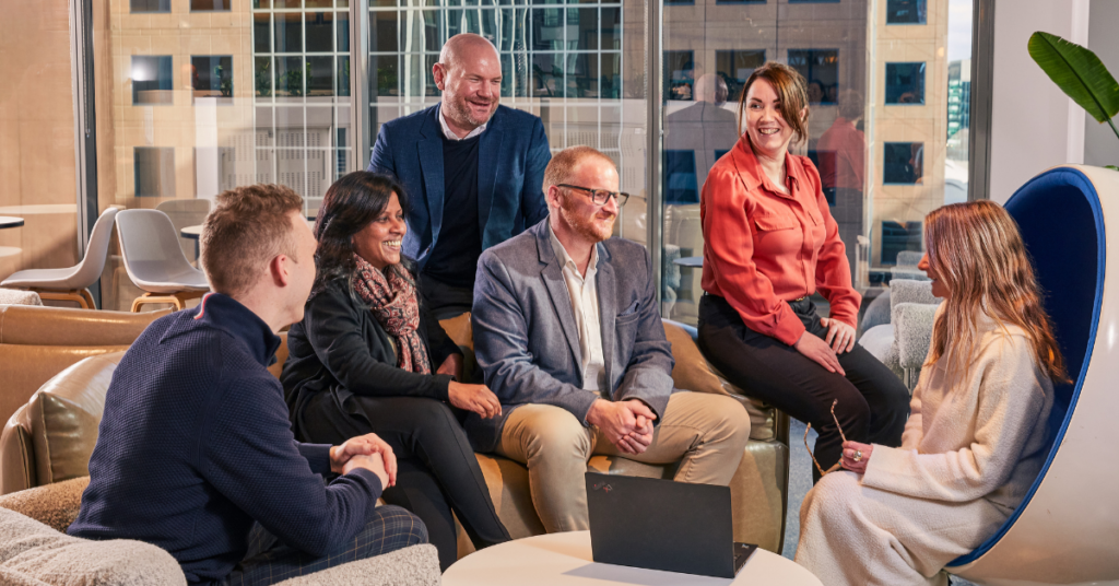 A group of people at BankVIC sitting in a room conversing and smiling.