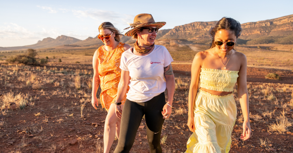 Three women travelling in a beautiful landscape. One of them wearing a white t-shirt with Intrepid logo printed on it