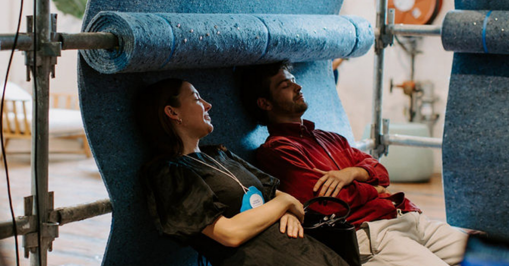 A woman and a man resting on a roll of teal coloured fabric