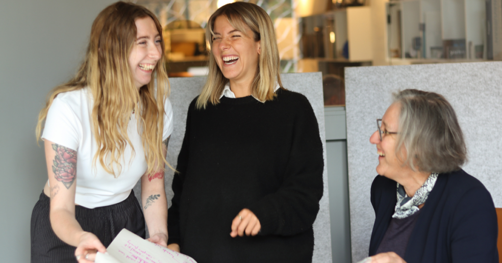 Three women employees at Juntos Marketing laughing and discussing marketing plan.