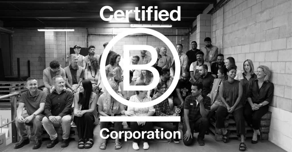 B Corp Epicurean dairy also known as The Collective NZ's team sitting , laughing and looking at each other. The image is black and white with Certified B Corporation logo in the centre