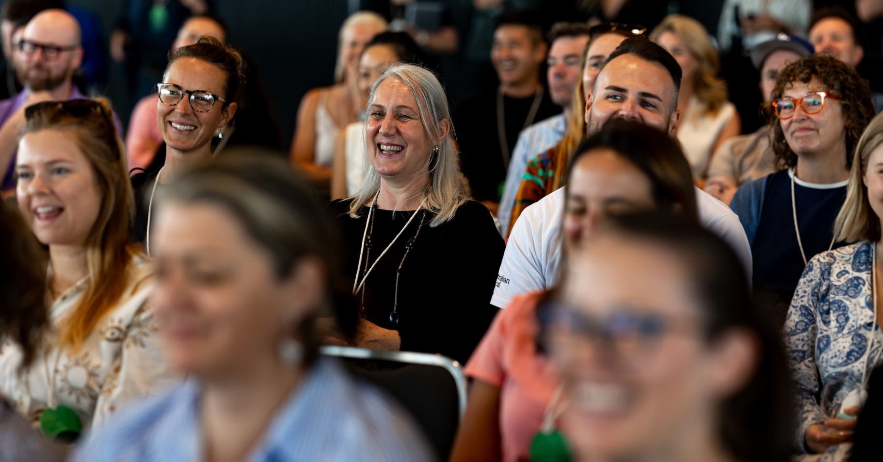 B Council members in the audience smile and laugh during a presentation or event, showing enthusiasm and engagement with the speaker or topic.