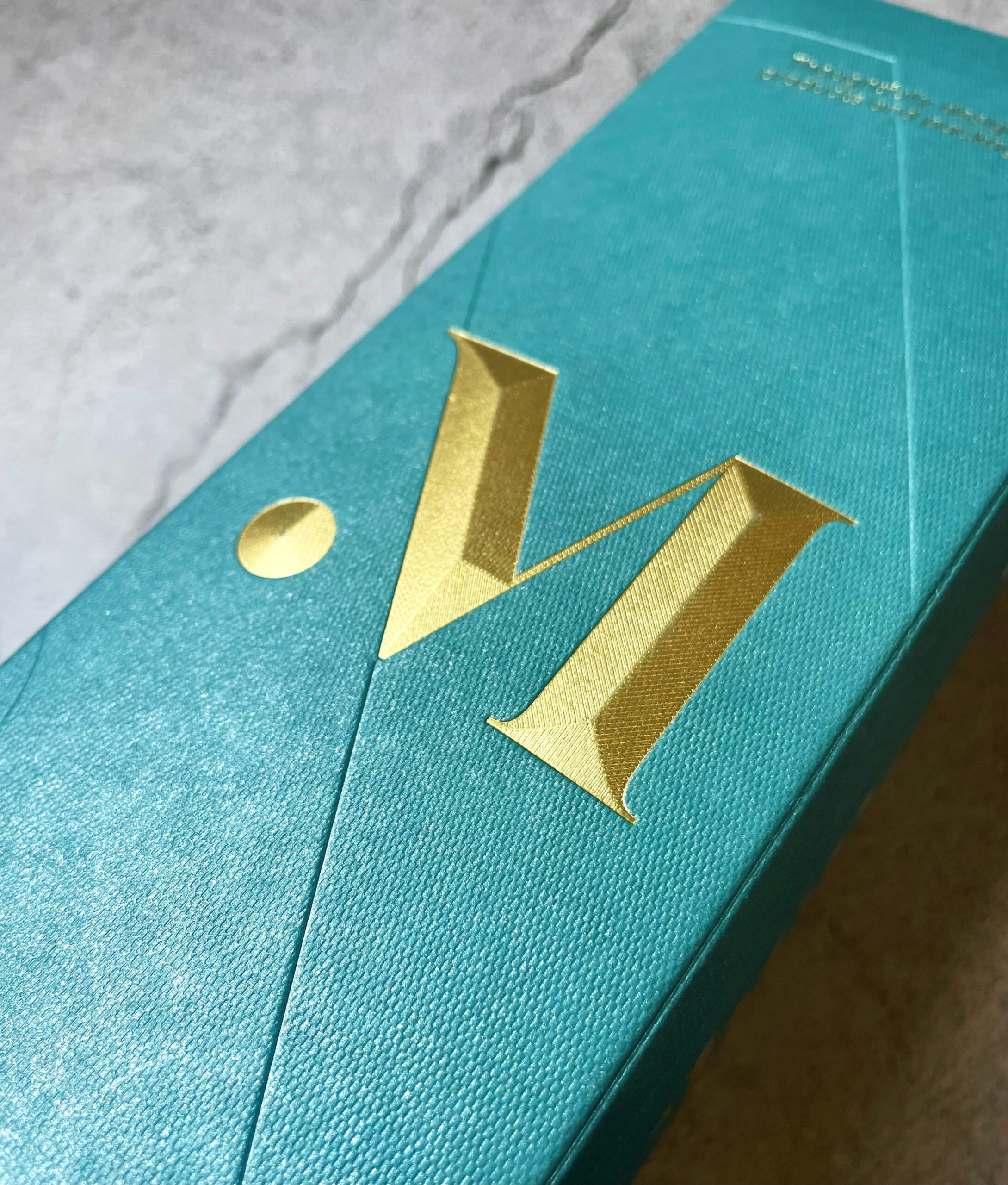 A close up of a gold logo on a teal wine box