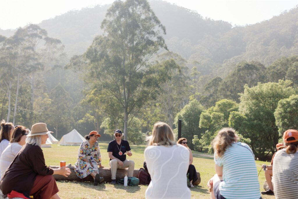 A group of people sat in a circle on logs, surrounded by hills.