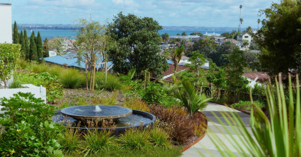 A landscaped garden on the top of a hill, with homes and the sea in the distance.