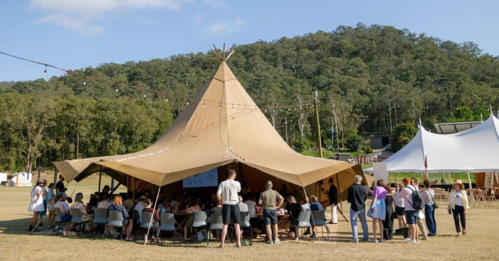 An audience listening to a presentation in a tent with hills behind.