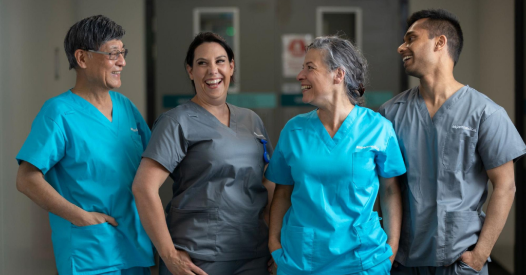 Four members of the Aspen Medical team smiling in a hospital setting in scrubs.