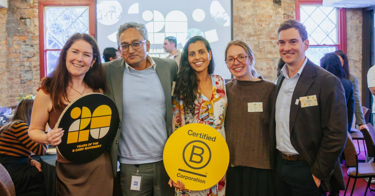 Vikram and Rachael with members of the B Lab AANZ team at a 20th anniversary event in Melbourne. Rachael is holding up a yellow B Corp logo sign.