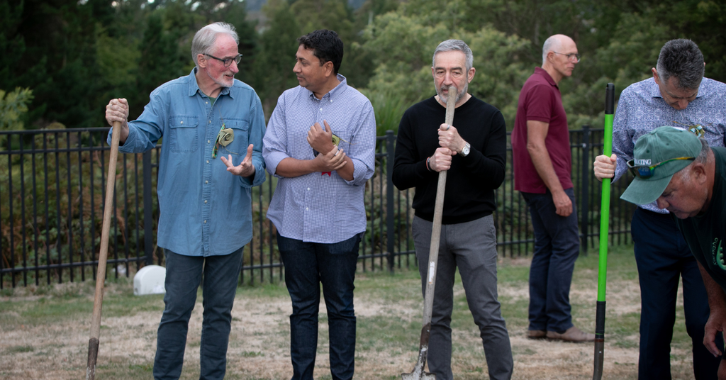 A group of men stand holding shovels as they complete a team building exercise. 